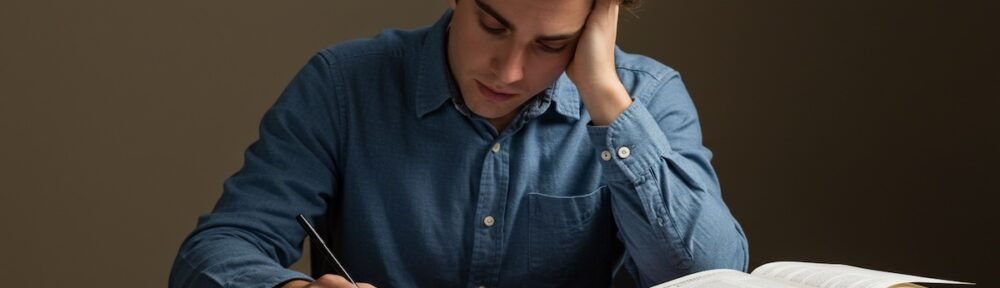 stressed-student-studying-cpa-exam-retake - CPA 2025 Requirements by State | CPA Exam and Accountant Education Frustrated accounting student studying for CPA exam retake with textbooks, calculator, and highlighters on desk.